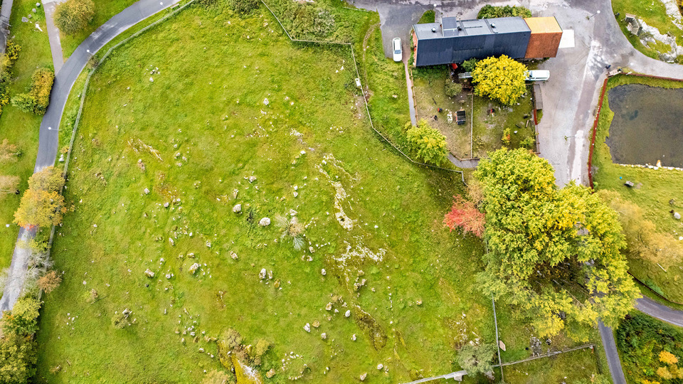 Flygbild över öppen gräsyta med stenar. Ett hus ovanifrån och vägar.
