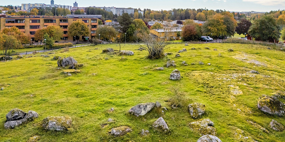 Kulle med stenar utspritt. Nedanför kullen finns bostadshus.